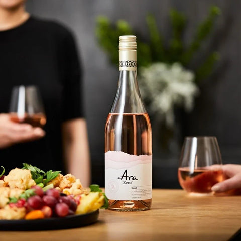 Butelka bezalkoholowego wina różowego Guiltfree Ara Zero Rosé z Marlborough na stole z przekąskami i kieliszkami.