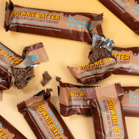 Guiltfree baton proteinowy Barebells Brownie Batter w czekoladowej polewie z chrupiącymi kawałkami na żółtym tle