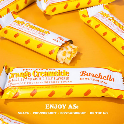 Baton proteinowy Guiltfree Barebells Orange Creamsicle w białej polewie z pomarańczową posypką na żółtym tle.