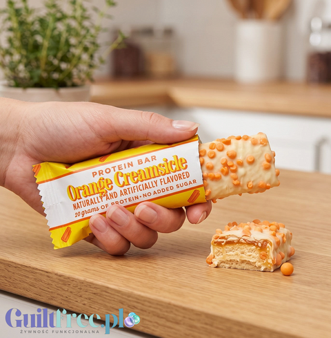 Baton proteinowy Guiltfree Barebells Orange Creamsicle w białej polewie z pomarańczową posypką trzymany w dłoni