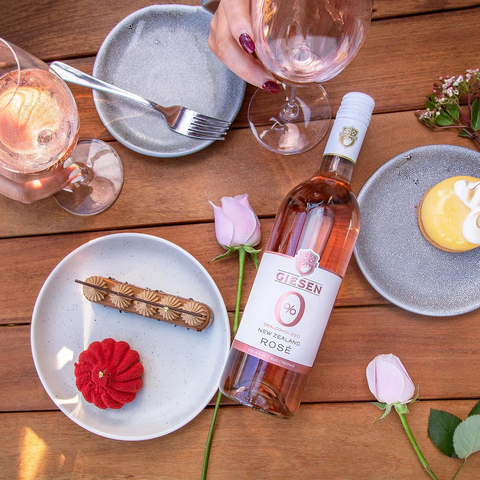 Butelka wina bezalkoholowego Guiltfree Giesen 0% Rose na drewnianym stole z deserami i kieliszkami