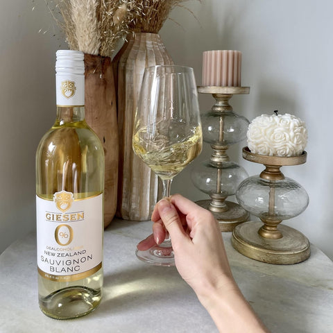 Butelka bezalkoholowego wina Giesen 0% Sauvignon Blanc i kieliszek wina w ofercie Guiltfree na marmurowym blacie.