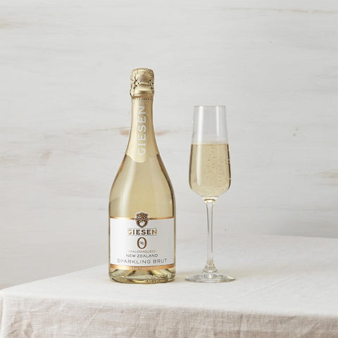 Butelka bezalkoholowego wina musującego Giesen Sparkling Brut 0% z kieliszkiem na białym stole