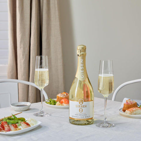 Butelka bezalkoholowego wina musującego Guiltfree Giesen Sparkling Brut z dwoma kieliszkami i sushi na stole.