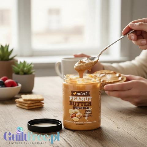 Guiltfree masło orzechowe Mixit Crunchy z kawałkami orzechów w szklanym słoiku nakładane łyżką na kanapkę