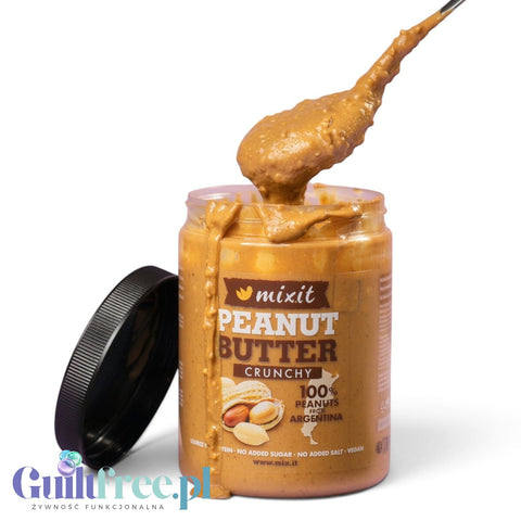 Słoik masła orzechowego crunchy Mixit od Guiltfree z łyżką nabierającą kremową masę z kawałkami orzechów