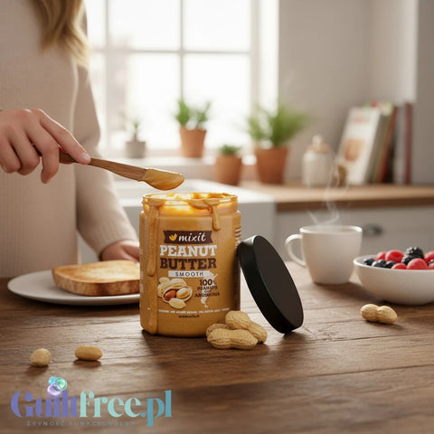 Słoik masła orzechowego Mixit Smooth marki Guiltfree na drewnianym stole z tostami i orzechami ziemnymi w tle