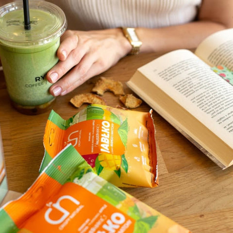 Guiltfree Crispy Natural musujące chipsy jabłkowe o smaku mango i matchy na drewnianym stole obok książki i napoju