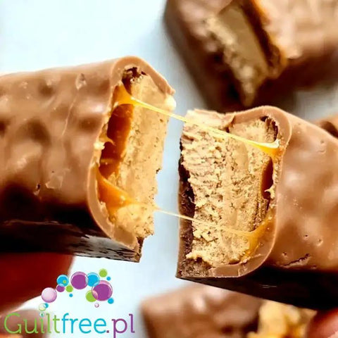 Przekrojony baton proteinowy Guiltfree Trec o smaku nugatu i karmelu z ciągnącym nadzieniem w mlecznej czekoladzie